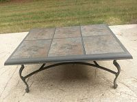 Photo showing full view of rectangular outdoor tile coffee table with metal legs on concrete surface outdoors with grass background.