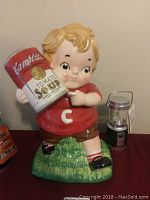 Full view of the Campbell's themed ceramic cookie jar shaped as a boy holding a tomato soup can, with LED lantern visible to the right.