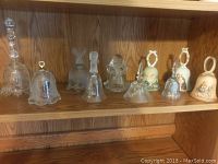 Front view of 10 glass and ceramic bells displayed on wooden shelves