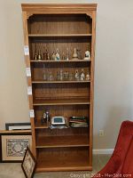 Front view of a tall wooden bookcase showing seven shelves with decorative top molding and corner brackets. Some items are on shelves but not included.