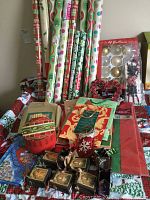 Photo showing 11 unopened rolls of wrapping paper with various holiday patterns, assorted decorative items including bows and small boxes, and a box of glass ornaments with gold spherical shapes.
