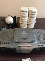 Photo showing top view of Koss AM/FM CD player stereo radio, Sony MDR-CD180 silver and black headphones, and white Right multimedia speakers with cords.