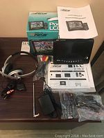 Full lot showing Prism portable digital LCD TV with screen, remote, manuals, cables, and box, alongside Logitech headphones.