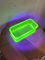 Rectangular uranium glass dish glowing bright green under UV highlighting ribbed sides and open top