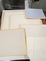 Stack of four mounted Aida cloth frames and loose fabric piece underneath