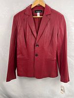 Front view of red leather jacket on hanger showing two-button closure, lapels, pockets, retail tag