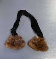 Full view of black velvet scarf with fur ends displayed flat