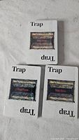 Front view of three sealed Trap Door decks showing white boxes with Trap Door graphic