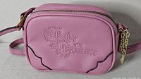Front view showing embossed logo, scalloped piping, zipper and charm