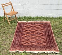 Full view of Bokhara wool rug placed on grass, chair for scale
