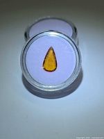 Front view of loose orange pear-cut sapphire in plastic gem jar