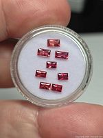 Seven rectangular pink-orange sapphires in circular gem case