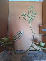 Front view of metal wall sconce showing leaf design and two candle cups
