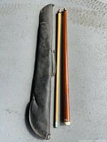 Pool cue separated into two pieces beside black case