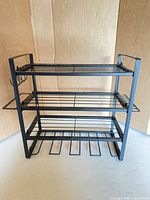 Front view of black metal 3-tier rack showing shelves and hooks