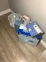 Lot overview showing foot spa box, neck massager box, blood pressure monitor box, motion alarm package and slow cooker