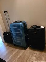 Three pieces of luggage standing upright: blue Samsonite hardshell, two black Jetstream softside cases