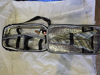 Open insulated picnic tote showing foil lining, two clear plastic wine glasses, plaid napkin, corkscrew