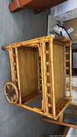Side view of rattan and bamboo two-tier tea cart showing lattice side panels, one large wooden wheel, shelf surfaces