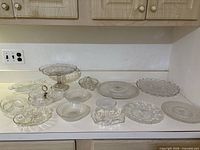 All 14 clear pressed/cut glass serving pieces displayed on countertop