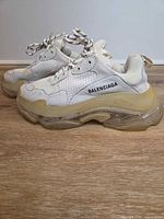 Left side view of both sneakers showing off-white leather/mesh uppers, Balenciaga logo and translucent sole