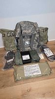 Full lot overview showing backpack, sealed JSLIST packages, gloves, overboots, hydration system, filter box, M8 paper, decon mitt
