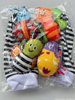 Front view of sealed package showing striped wrist rattles, socks, and colorful plush insect heads