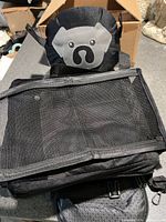 Black pet booster seat folded showing mesh top, dog-face panel, straps