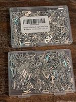 two clear plastic cases filled with silver alphabet charms, barcode on one