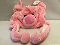 Front view of pink plush pig hat with ear flaps and pom-poms