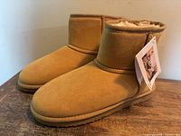 Side view of both tan Zizor ankle slipper boots with tags attached