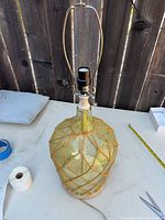 Full view of lamp showing glass body with jute netting, wood neck, harp and cord