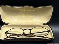 Eyeglass frames resting inside open Giorgio Armani case showing gold logo interior