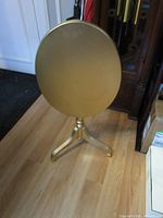 Front view of gold oval tilt-top side table in raised position