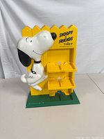 Front view of yellow Snoopy & Friends Timex display stand with green base and three shelves