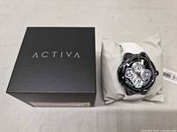 Closed black Activa box beside wrapped watch on cushion