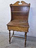 Full view front of light brown solid wood writing desk showing shelf, lift-top surface, turned legs