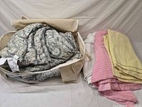 Comforter folded in storage bag next to stacked blankets and sheet