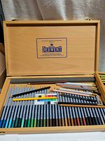 Open wooden case showing lower tray of Derwent Artists pencils, loose pencils and colour card on top