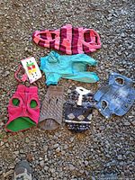 All six dog sweaters, denim vest, bead collar and hair bows laid out on gravel