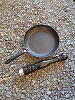 T-Fal non-stick frying pan and large black pepper grinder on gravel surface