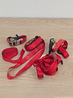 Overview of three coiled red ratchet straps with hooks on light wood surface