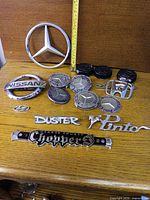 All emblems and badges laid out on wood surface with measuring tape for scale