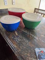 Red, blue and green bowls with lids, nested on countertop