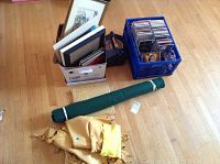 Photo of box with various picture frames and a crate with CDs and DVDs, plus rolled green fabric and leather chamois cloths on the floor.