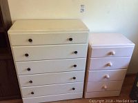 Photo showing the two painted wood chests of drawers, one larger with five drawers and brown knobs, one smaller with three drawers and light-colored knobs placed side by side.