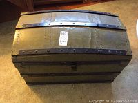 Top external view of a vintage dome top storage trunk with a green exterior and black riveted metal straps showing wear and dents.
