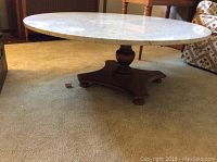 Full view of the round coffee table showing the marble top and wood base on carpet.
