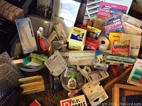 Photo showing a collection of paper products including binders, folders, Post-It notes, tape dispensers, and small office tools piled on a floor surface.