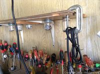 View of screwdrivers with diverse handles stored upright on pegboard hooks against a wood panel wall.